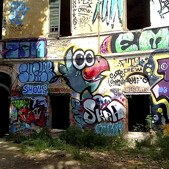 Fotografía de la fachada llena de grafitis de un balneario muy importante que fue abandonado. Está en ruinas pero todas sus paredes están pintadas con colores llamativos y expresiones artísticas de grafiteros.